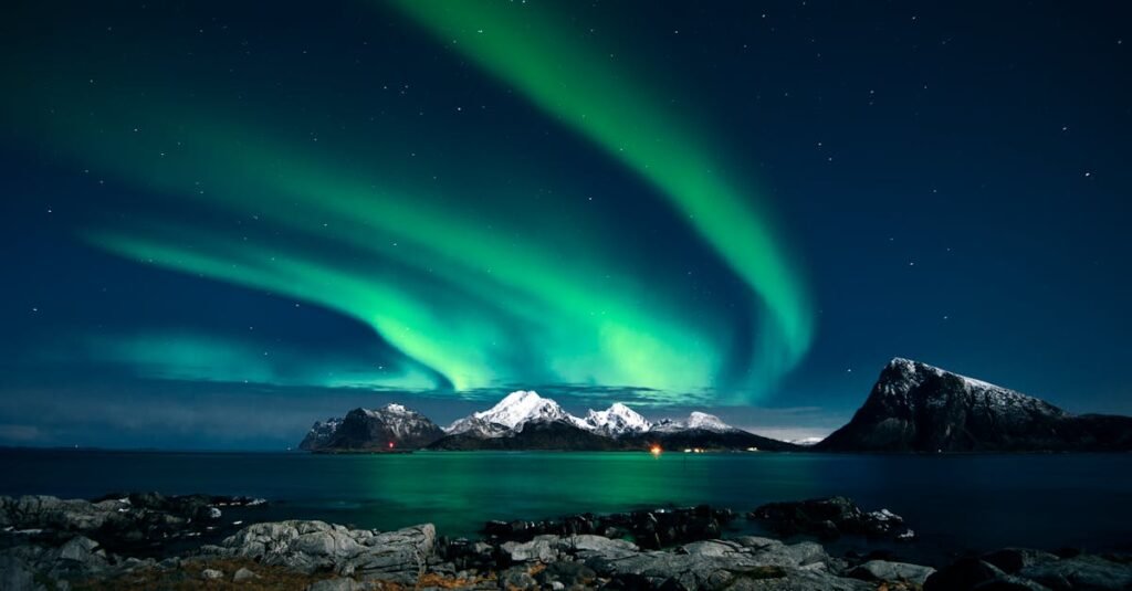 Breathtaking northern lights display over snow-covered mountains and serene waters in Lofoten, Norway.